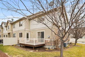 Rear view of property with fence, stone siding, a lawn, a wooden deck, and stucco siding