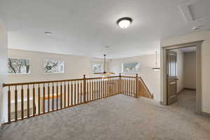 Hall with an upstairs landing, carpet, a textured ceiling, and baseboards