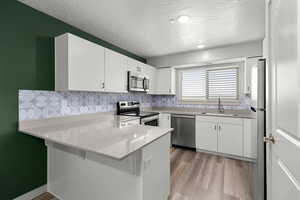 Kitchen with a sink, a textured ceiling, a peninsula, and stainless steel appliances