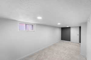 Below grade area featuring recessed lighting, light colored carpet, a textured ceiling, and baseboards