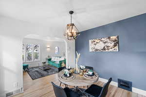 Dining space with arched walkways, wood finished floors, visible vents, and baseboards