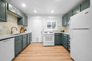 Updated Kitchen with white appliances, blue-green painted cabinetry, elegant marble tile backsplash, quartz countertops, and LVP flooring.