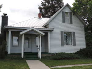 Bungalow-style home with a chimney, covered porch, and metal roof
