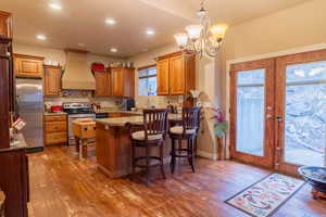 Kitchen with stainless steel appliances, premium range hood, wood-type flooring, and a peninsula