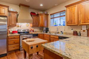 Kitchen with appliances with stainless steel finishes, wood finished floors, premium range hood, a sink, and recessed lighting