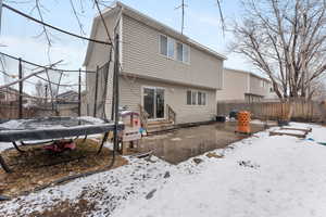 Snow covered rear of property featuring entry steps, a patio, a fenced backyard, a trampoline, and cooling unit