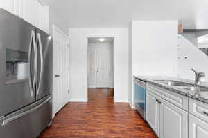 Kitchen featuring a sink, white cabinets, appliances with stainless steel finishes, light countertops, and dark wood finished floors