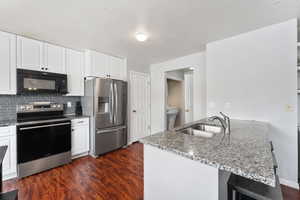 Kitchen with light counters, dark wood-style floors, stainless steel appliances, decorative backsplash, and a sink