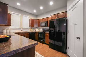 Kitchen featuring black appliances, decorative backsplash, dark countertops, light wood-style flooring, and recessed lighting