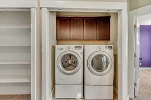 Clothes washing area with baseboards, independent washer and dryer, cabinet space, and light colored carpet