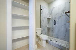 Bathroom featuring a marble finish shower, tile patterned floors, and a walk in closet