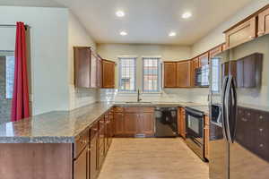 Kitchen featuring a sink, light wood-type flooring, black appliances, brown cabinetry, and dark countertops