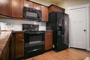Kitchen with black appliances, light wood-type flooring, and tasteful backsplash