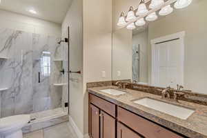 Bathroom with a marble finish shower, double vanity, a sink, and toilet