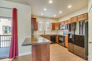 Kitchen featuring brown cabinets, light wood-style flooring, a sink, a peninsula, and black appliances