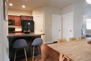 Kitchen featuring black appliances, a breakfast bar, backsplash, dark wood finished floors, and dark countertops