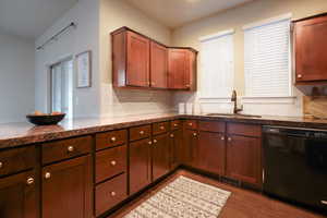 Kitchen featuring black dishwasher, tasteful backsplash, dark wood finished floors, dark stone counters, and a peninsula