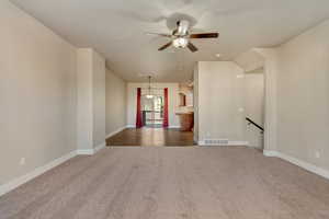 Unfurnished living room featuring a ceiling fan, baseboards, visible vents, and carpet flooring