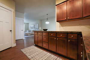 Kitchen featuring dark wood finished floors, open floor plan, a peninsula, hanging light fixtures, and dark stone countertops