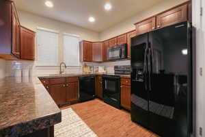 Kitchen featuring black appliances, light wood-type flooring, tasteful backsplash, recessed lighting, and dark countertops