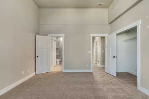 Unfurnished bedroom featuring carpet floors, visible vents, a towering ceiling, ensuite bathroom, and baseboards