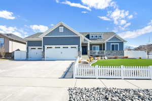 Craftsman inspired home with driveway, stone siding, a fenced front yard, and a porch