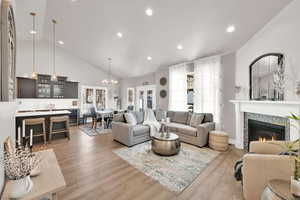 Living room featuring light wood finished floors, a tiled fireplace, wine cooler, high vaulted ceiling, and recessed lighting