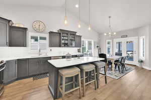 Kitchen featuring light wood finished floors, decorative backsplash, glass insert cabinets, a kitchen breakfast bar, and light countertops