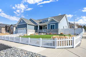 View of front of property featuring driveway, stone siding, a fenced front yard, an attached garage, and board and batten siding