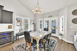 Dining space with lofted ceiling, light wood-style flooring, an inviting chandelier, beverage cooler, and baseboards