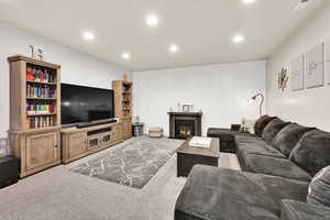 Living area with carpet, a glass covered fireplace, visible vents, and recessed lighting