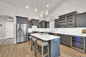 Kitchen with light wood-style flooring, beverage cooler, a breakfast bar, a sink, and appliances with stainless steel finishes