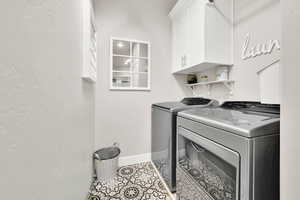 Clothes washing area with cabinet space, washing machine and dryer, light tile patterned floors, and baseboards