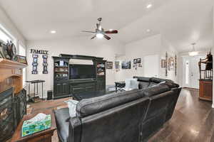 Living area with lofted ceiling, ceiling fan, a fireplace, and dark wood-style flooring