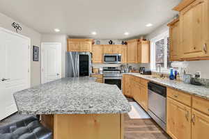 Kitchen featuring dark wood-style floors, a breakfast bar, stainless steel appliances, light brown cabinets, and a sink