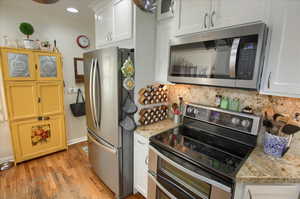 Kitchen with white cabinets, light wood finished floors, stainless steel appliances, and backsplash