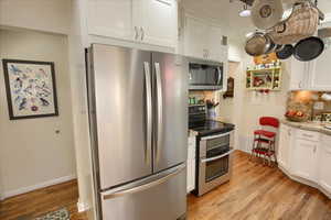 Kitchen featuring stainless steel appliances, tasteful backsplash, light wood-type flooring, and white cabinetry