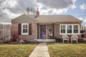 View of front of home with brick siding, a shingled roof, fence, a chimney, and a front yard