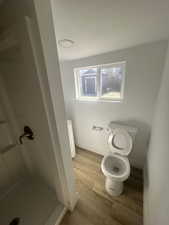 Bathroom with a stall shower, wood finished floors, toilet, and baseboards