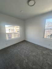 Empty room with baseboards, a textured ceiling, dark carpet, and a healthy amount of sunlight