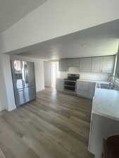 Kitchen with appliances with stainless steel finishes, wood finished floors, a sink, and gray cabinetry