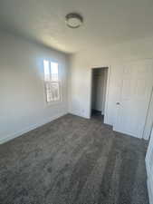 Unfurnished bedroom featuring a closet, baseboards, dark colored carpet, and a textured ceiling