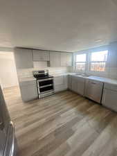 Kitchen featuring range with two ovens, gray cabinets, a sink, light wood-type flooring, and dishwasher