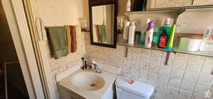 Bathroom with decorative backsplash, vanity, toilet, and tile walls