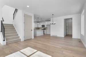 Unfurnished living room with light wood-type flooring, visible vents, a notable chandelier, and stairway