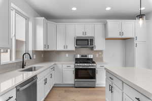 Kitchen featuring decorative light fixtures, light wood finished floors, appliances with stainless steel finishes, white cabinets, and a sink