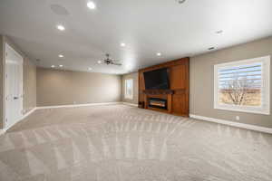 Unfurnished living room with baseboards, visible vents, a glass covered fireplace, and light colored carpet