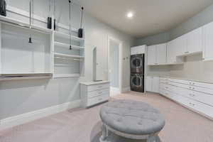 Walk in closet with stacked washer and clothes dryer and light colored carpet