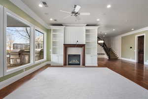 Living area with dark wood-style floors, a glass covered fireplace, visible vents, and ornamental molding