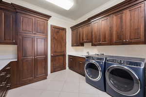 Clothes washing area with ornamental molding, cabinet space, independent washer and dryer, and light tile patterned floors